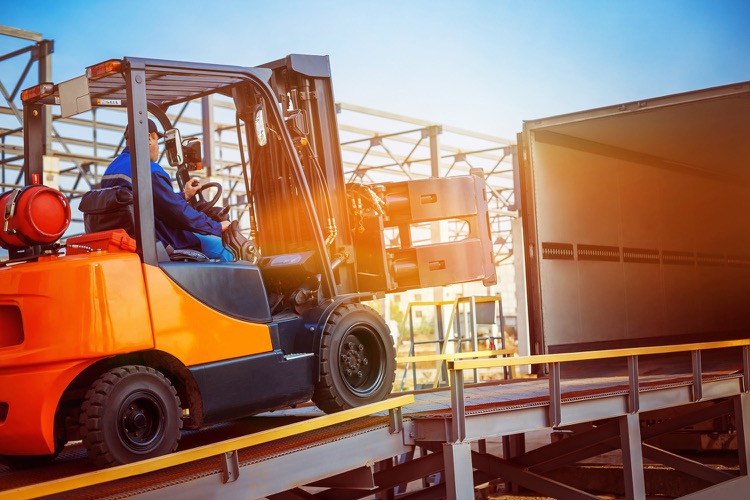 A forklift driving up a ramp loading equipment onto a trailer.