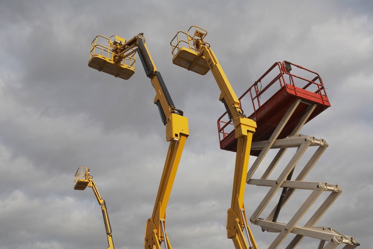 Three boom lifts and a scissor lift fully extended into a cloudy sky.