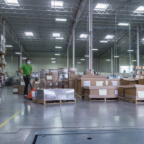 A worker operating a pallet jack in a wearhouse full of boxes.